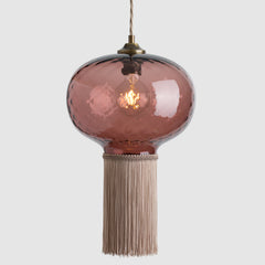Pink glass pendant light with fabric fringe on a white background