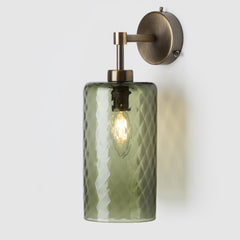 Wall-mounted light fixture with green glass shade and brass fixture on a white background