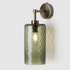 Wall-mounted light fixture with green glass shade and brass fixture on a white background