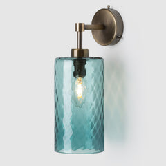 Wall-mounted light fixture with teal glass shade and brass fixture on a white background