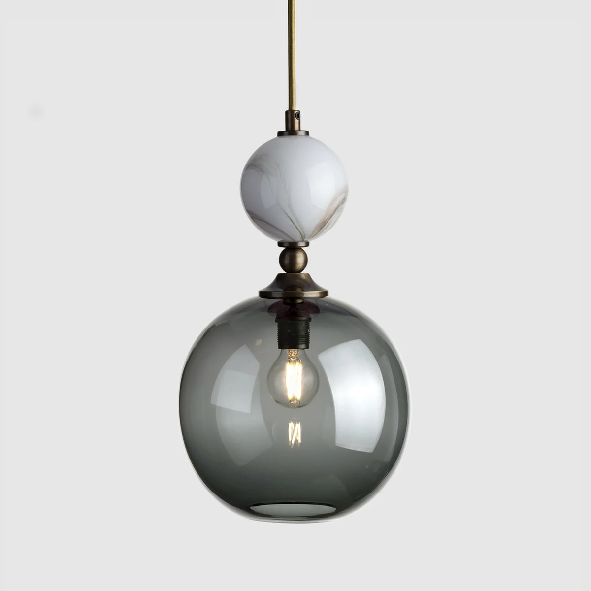 Hand made pendant light with a grey glass globe and a marble sphere on top, with antique brass metal and gold fabric cable
