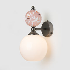 Wall-mounted light fixture with a decorative pink glass shade on a white background