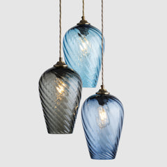 Three twisted optic glass pendant lights in blue, grey, and blue on a light grey background