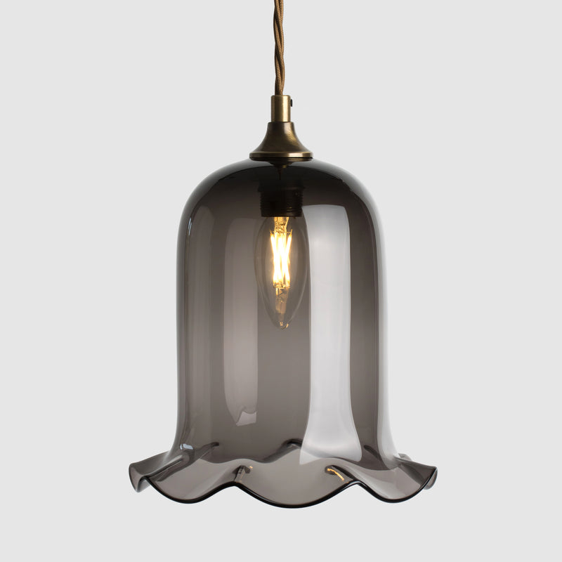 Bell shaped coloured glass light shade with frilled bottom on twisted fabric covered flex