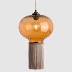Suspension light with amber glass shade and pale pink fabric fringe on a white background