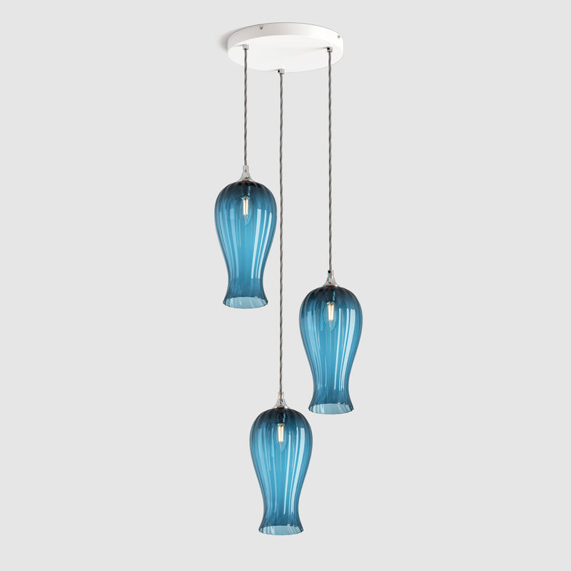 Group of Long ribbed blue coloured glass decorative pendant lights with brass fitting and fabric covered flex, hanging on a ceiling plate